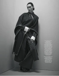 Model leaning against a corner wearing a dark coat with white cuffs and trousers for Madame Germany Sacre Coeur editorial