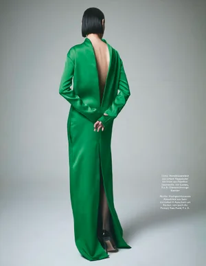 A model from the back wearing a long green dress with a plunging open back against a grey studio backdrop.