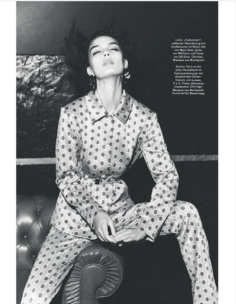 A model poses in a patterned suit against a dark backdrop, showcasing fashion and style in a studio environment with natural light.
