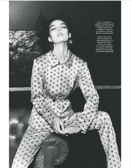 A model poses in a patterned suit against a dark backdrop, showcasing fashion and style in a studio environment with natural light.