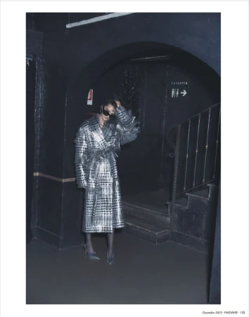 Woman in metallic plaid coat posing in dark archway near stairs. Fashion shot featuring sunglasses, heels, and cool toned aesthetic.