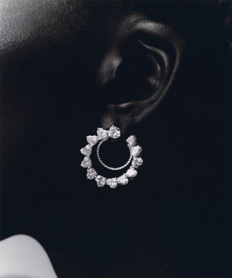 Close-up of a person's ear wearing circular diamond earrings on a dark background, jewellery design for beauty and fashion concepts.