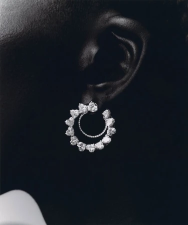 Close-up of a person's ear wearing circular diamond earrings on a dark background, jewellery design for beauty and fashion concepts.