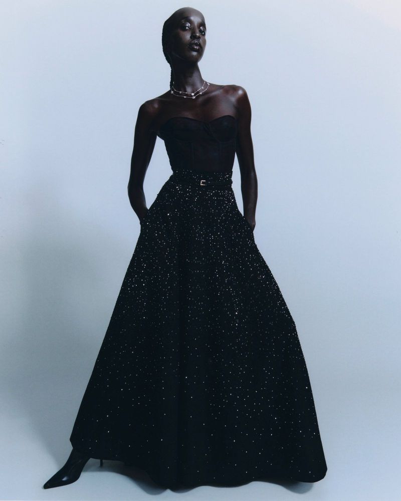 Model Nyaueth Riam wearing a black strapless gown and necklace against a plain grey background