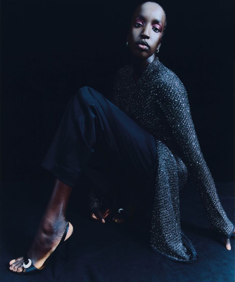 Woman in stylish shimmer top and pants posing indoors against dark background. Fashion shot with dramatic lighting and elegant simplicity.