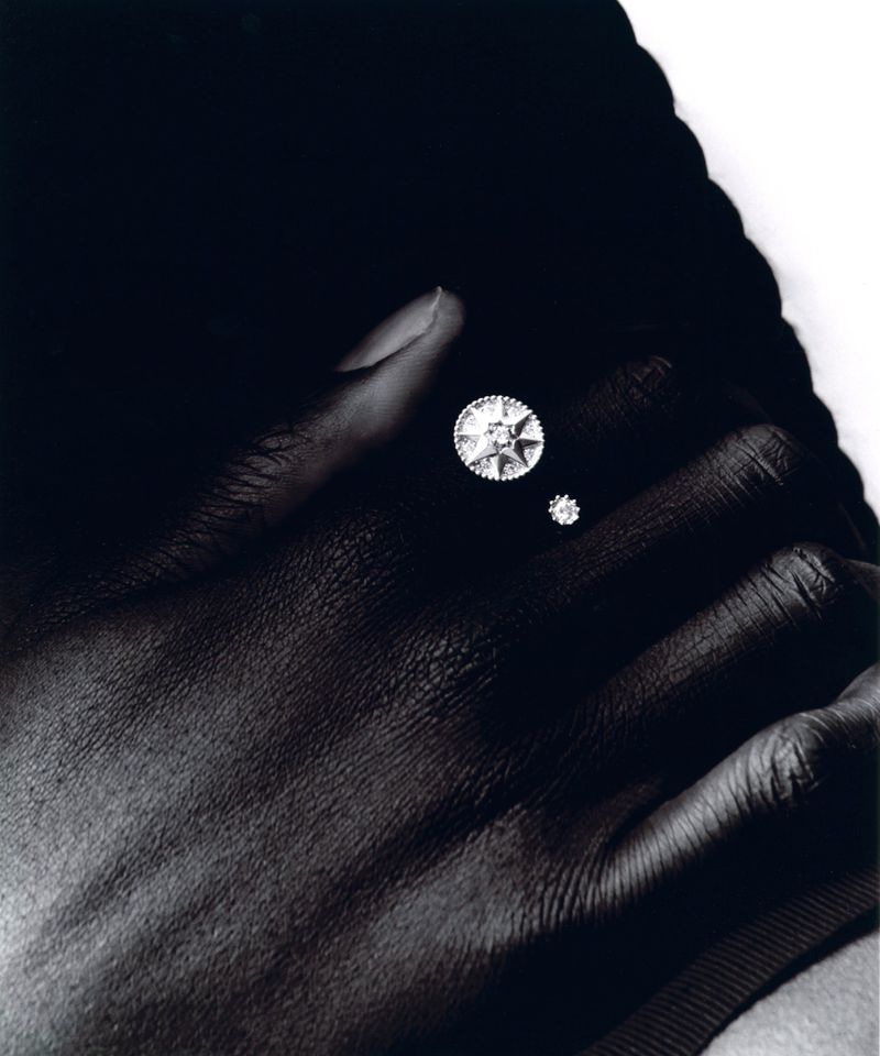 Close-up of a person's hand with two round cut diamonds on their fingers, set against a stark black-and-white backdrop.