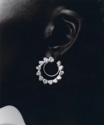 Close-up monochrome portrait of a person wearing an intricate diamond earring on their earlobe against a dark background.