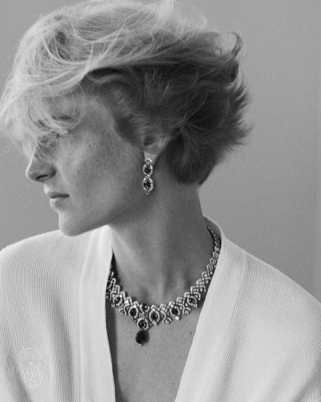 Black and white portrait of an adult woman with short blonde hair, wearing a white robe, statement earrings, and a diamond necklace.