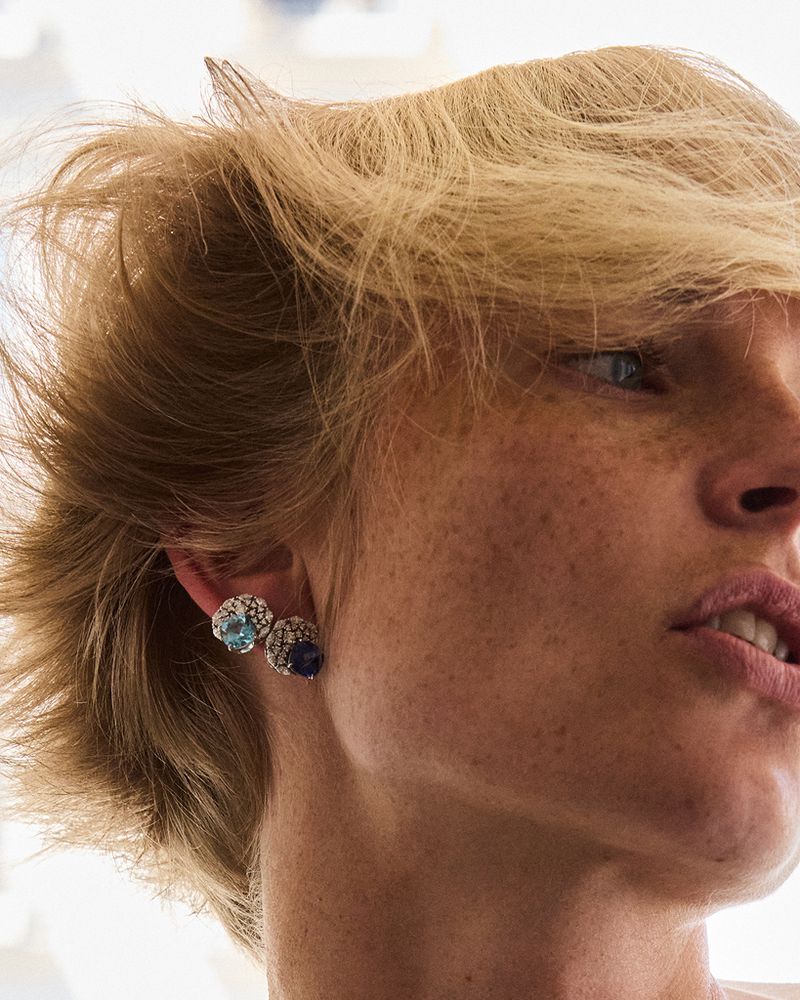 Close-up studio shot of a blonde adult female's face, freckles, jewelry earrings, with a blurred neutral background and soft diffused lighting.