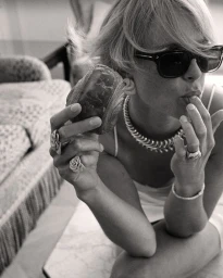 Model wearing dark sunglasses and chunky jewellery holding a pastry in a black and white editorial photograph for Madame Figaro.