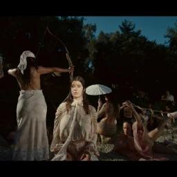 Group of women outdoors in a park setting, with one holding a bow and arrow and another seated in the center.