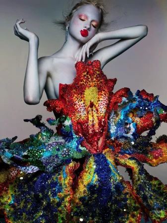 Model Kai Schreiber in an ornate embellished floral dress with bold red lips against a neutral gradient background.