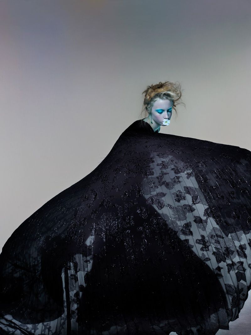 Model Kai Schreiber in a billowing black gown with bright blue eye makeup holding a flower for V Magazine by Nick Knight