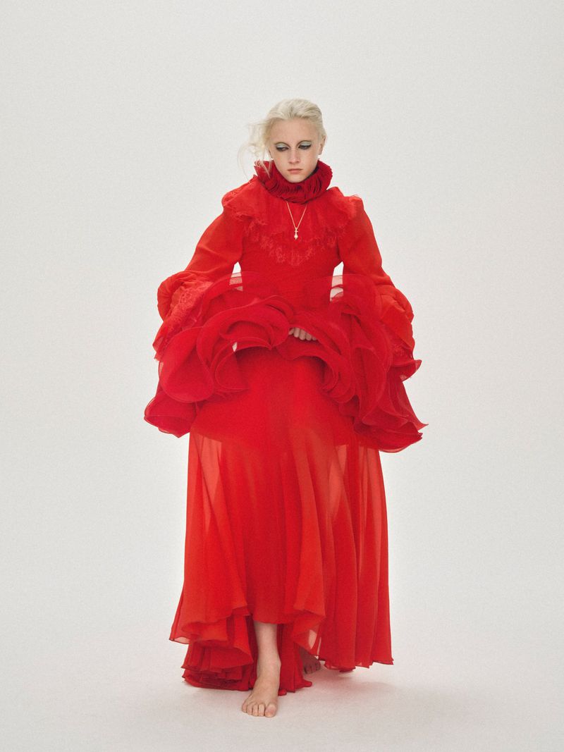 Young woman in a flowing red gown with ruffled sleeves and collar poses barefoot against a seamless white background.