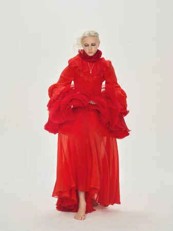 Young woman in a flowing red gown with ruffled sleeves and collar poses barefoot against a seamless white background.