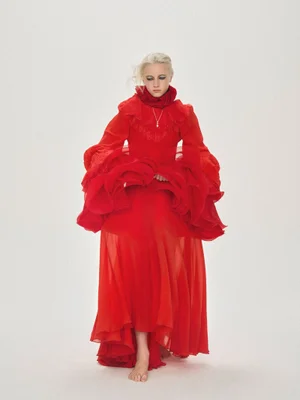 Model wearing a vibrant red ruffled dress standing against a plain light background