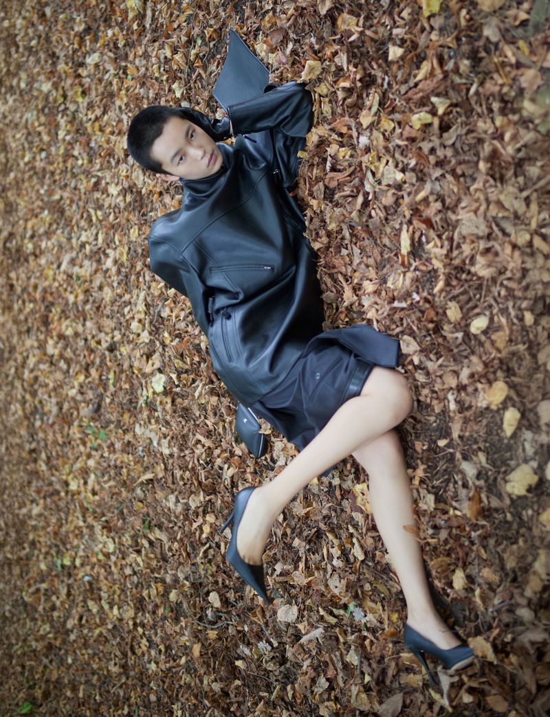 Woman in black dress and heels lying on fallen autumn leaves. Fashion shot with natural light and warm colors in a nature setting.