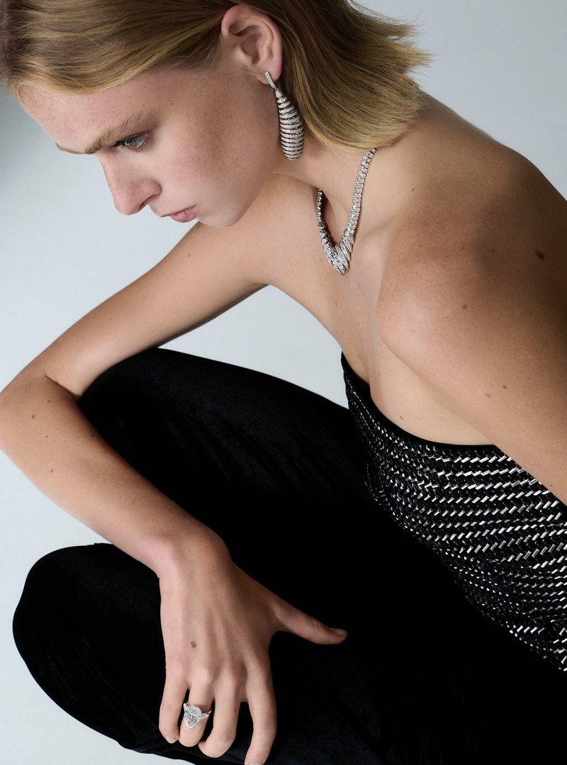 Woman with blonde hair poses in a studio wearing a black and silver strapless top, ring, and jewelry set against a white background.