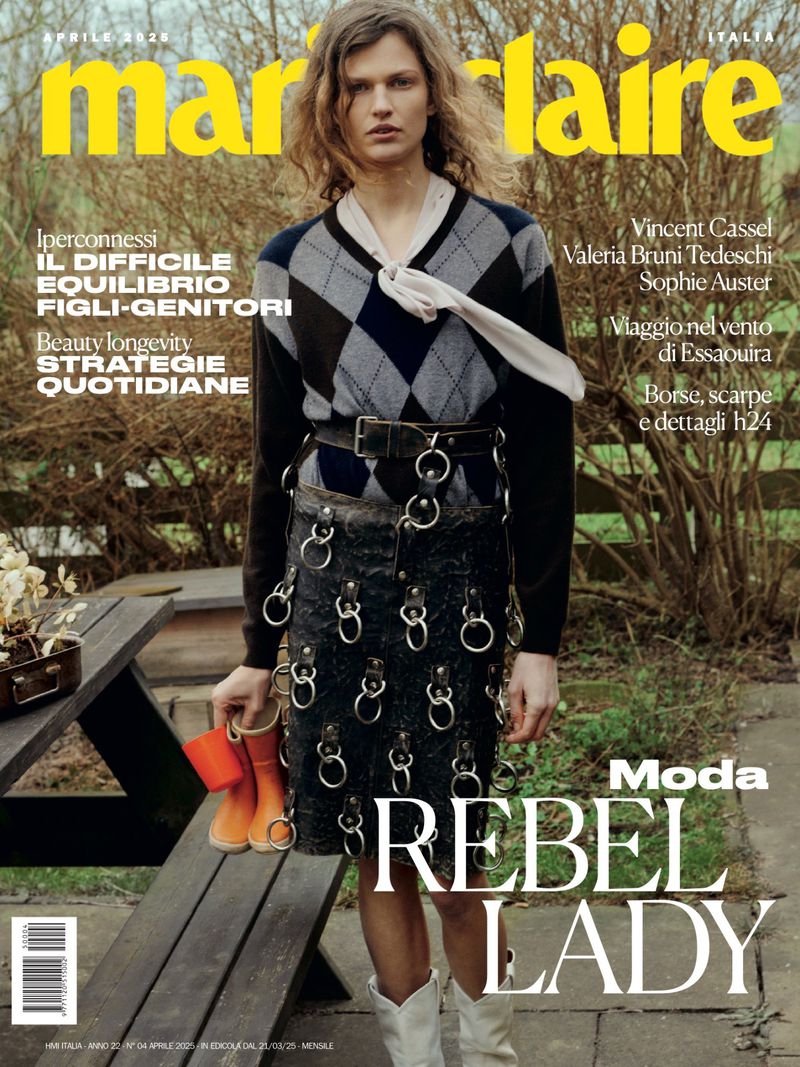 Marie Claire Italia cover featuring a fair-skinned model in an argyle sweater, ringed skirt, and cowboy boots holding orange rain boots, outdoors.