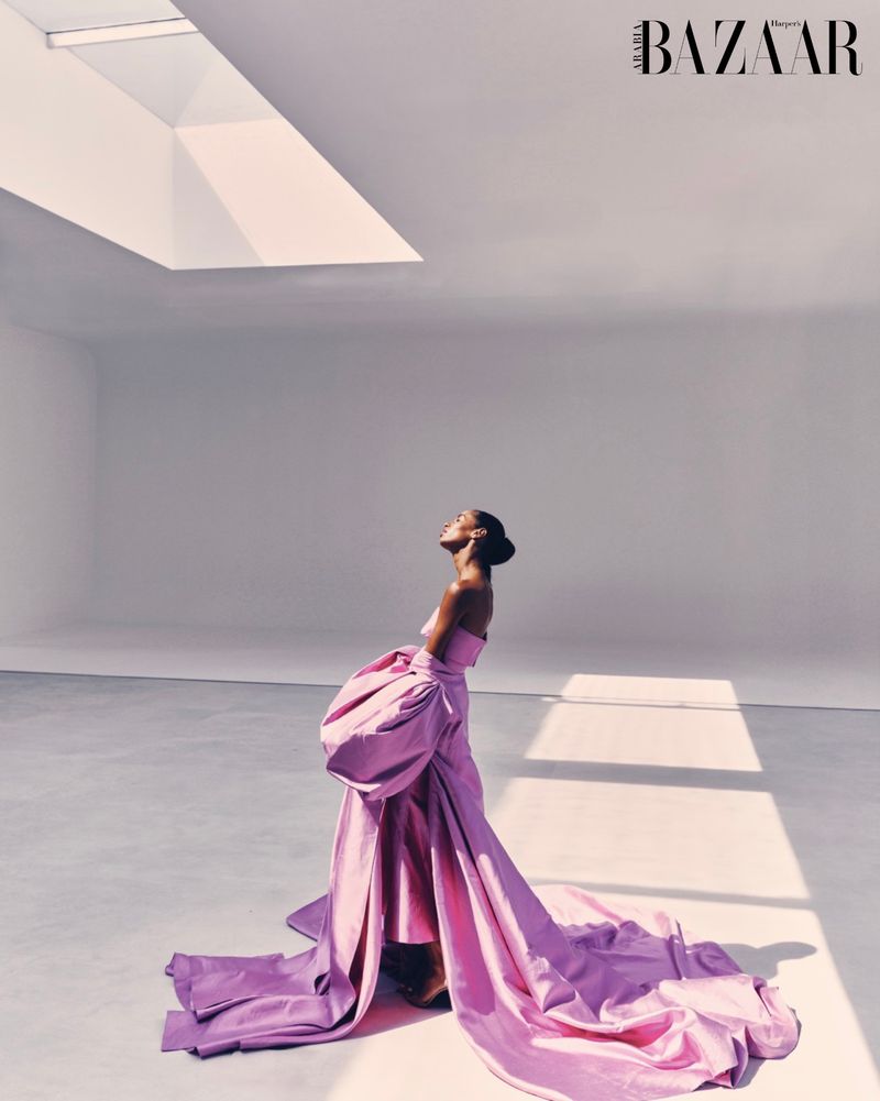 Elegant woman in lilac strapless gown with oversized bow poses in a bright white studio with natural light. Fashion editorial shot.