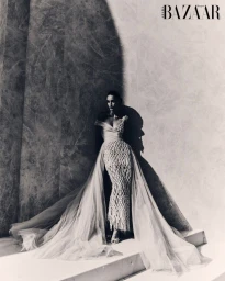 Model standing on stone steps in an elaborate textured evening gown with a flowing tulle overskirt for Harper's Bazaar Arabia.