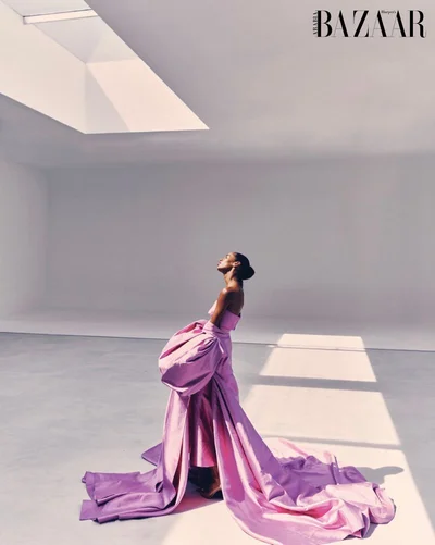 A model standing in a large minimalist room wearing a voluminous pink gown under a skylight.