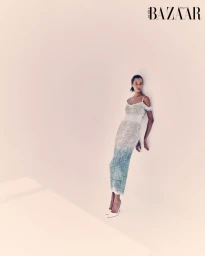 Model in a textured midi dress leaning against a plain wall for Harper's Bazaar Arabia