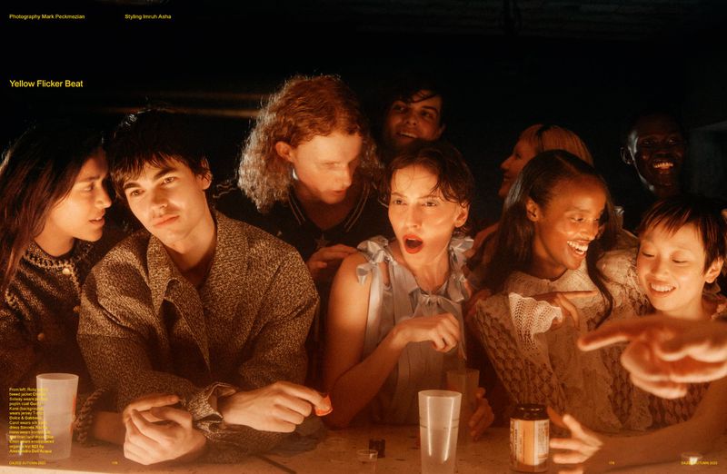 A diverse group of eight young adults are gathered around a table in a dimly lit setting, engaged in conversation and laughter.