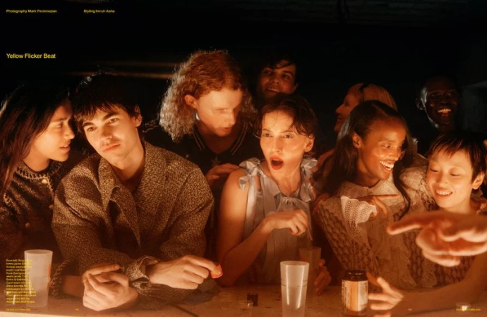 A diverse group of eight young adults are gathered around a table in a dimly lit setting, engaged in conversation and laughter.