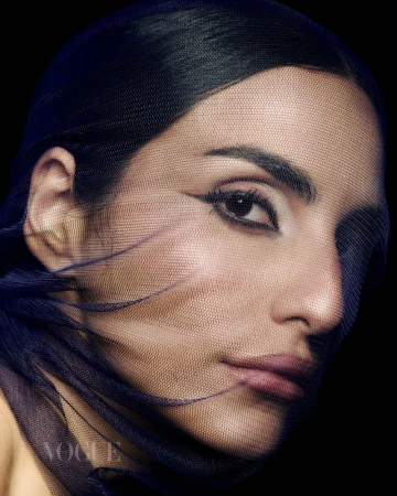 Close-up portrait of a woman with dramatic eye makeup, partially veiled in a dark blue mesh against a stark black backdrop.