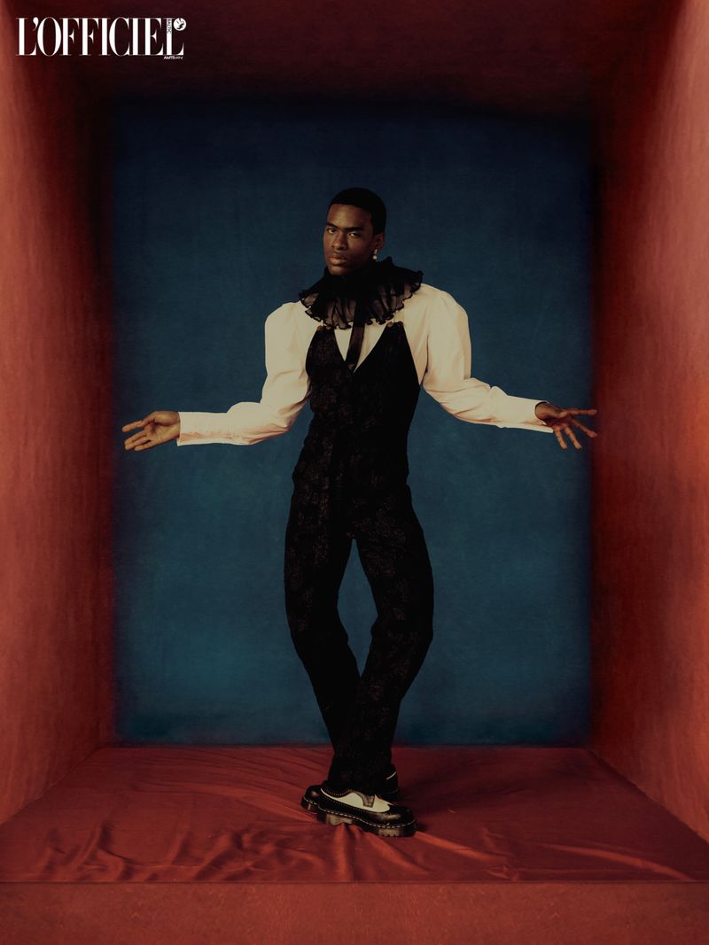 Man in black and white fashion posing in a box studio setting. Modern editorial look with puffy sleeves and platform shoes.