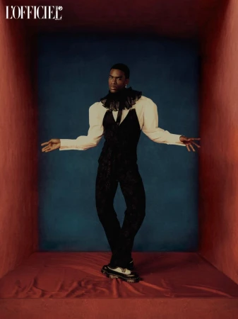Man in black and white fashion posing in a box studio setting. Modern editorial look with puffy sleeves and platform shoes.