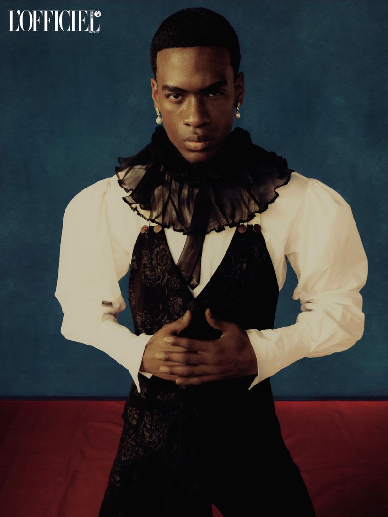 Portrait of a black man wearing a white shirt with ruffled collar and black vest for L'Officiel Baltics.