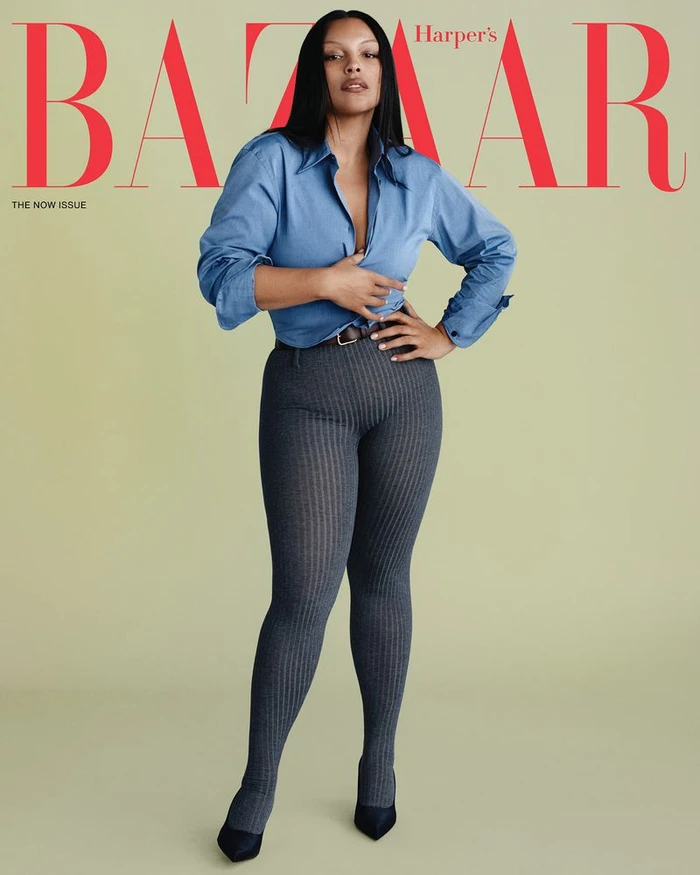 Model Paloma Elsesser in a blue button-down shirt and grey leggings against a solid backdrop for Harper's Bazaar US.