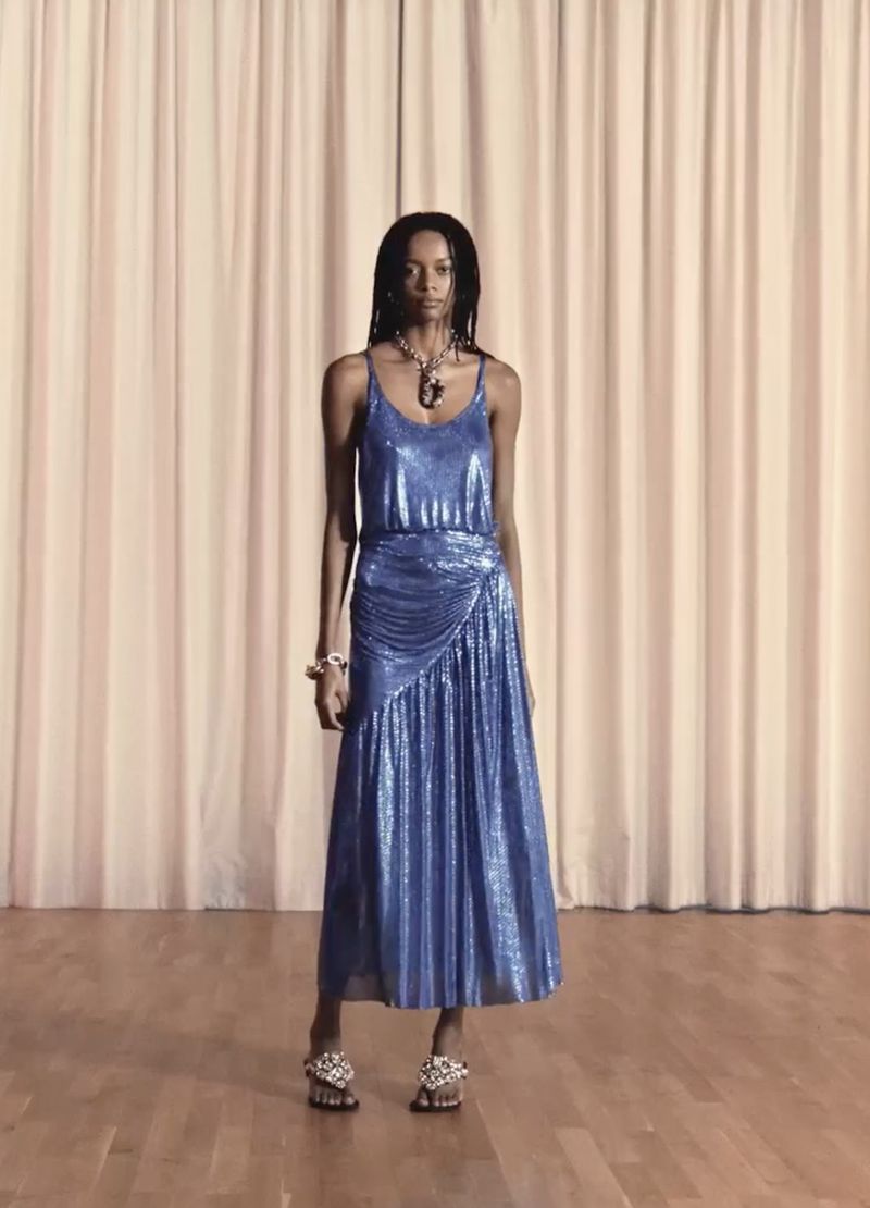 Model wearing a blue metallic midi dress standing before pale curtains in the Rabanne Party Collection 2025 campaign.
