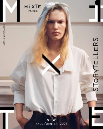 Editorial fashion shot: A woman with fair skin, wearing a white hooded garment and shirt, poses against a white backdrop with magazine graphics.