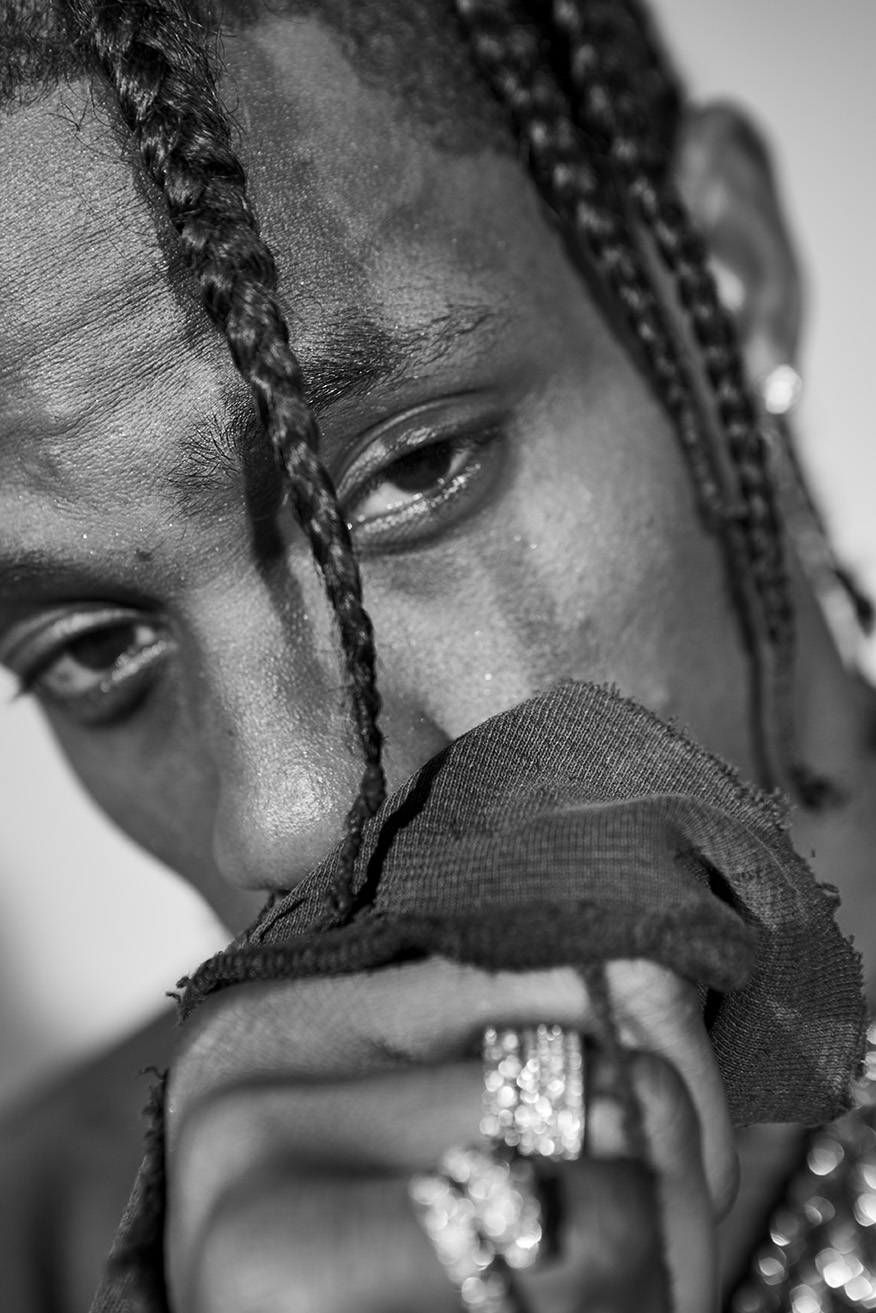 Close-up black and white portrait of a man with braided hair covering his face with a piece of cloth and wearing rings.