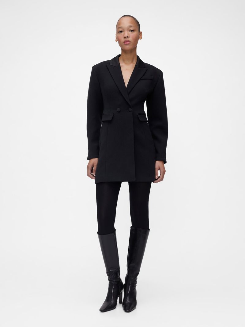 Model wearing a black tailored blazer dress and tall leather boots against a white seamless background for Gap.