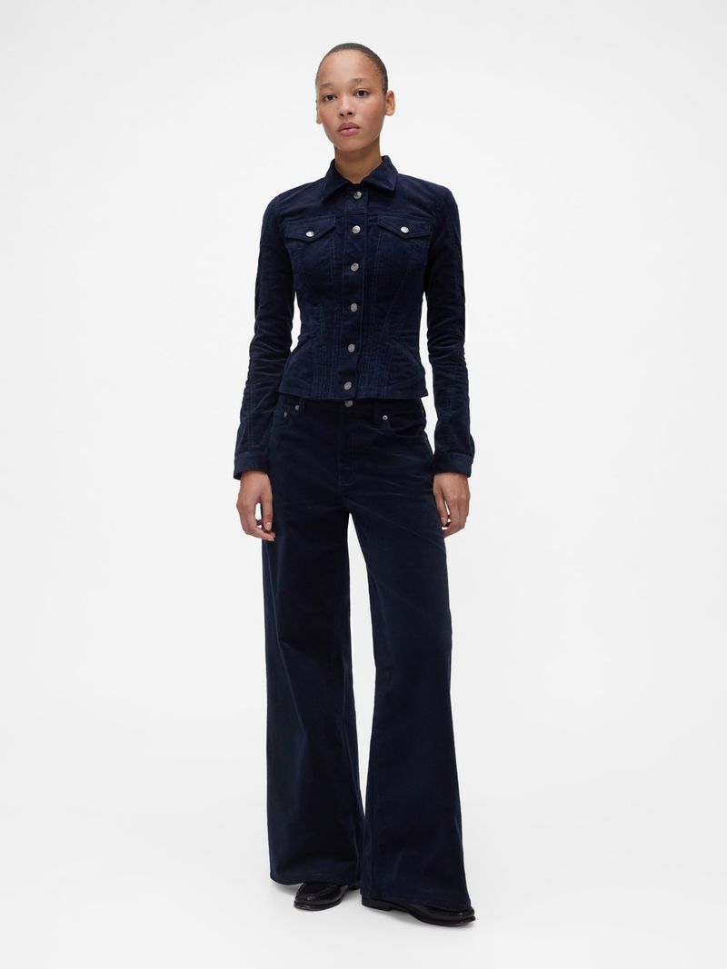 Full-length shot of a woman in a dark blue corduroy jacket and matching pants against a bright white seamless backdrop in a photo studio.