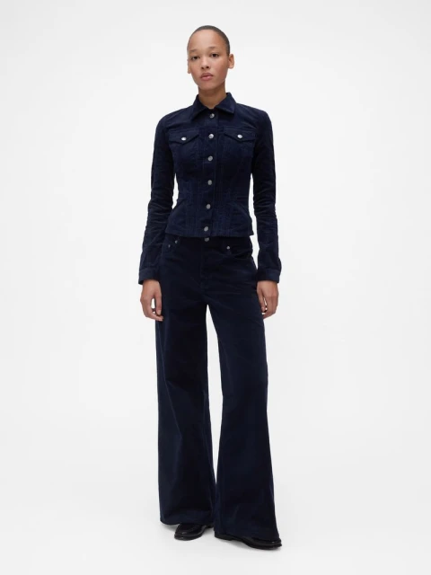 Full-length shot of a woman in a dark blue corduroy jacket and matching pants against a bright white seamless backdrop in a photo studio.