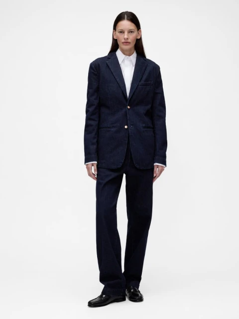 Full-length shot of an adult female with straight brown hair, wearing a navy blue blazer, white shirt, and pants against a white backdrop.