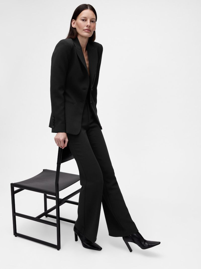 Model in a black suit leaning against a black chair against a bright white background