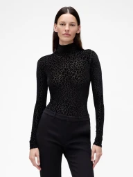 Model wearing a black patterned turtleneck top and black trousers against a plain white background