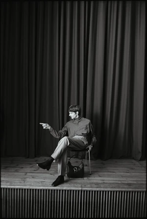 Monochrome fashion portrait of a man seated on a chair pointing sideways against heavy curtain background for Best Secret Campaign.