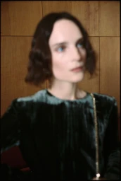 Softly blurred portrait of a woman with dark wavy hair wearing a dark velvet top against wooden paneling.
