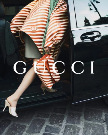 Model stepping out of a dark car wearing a striped coat and holding a matching handbag for Gucci Cruise 26