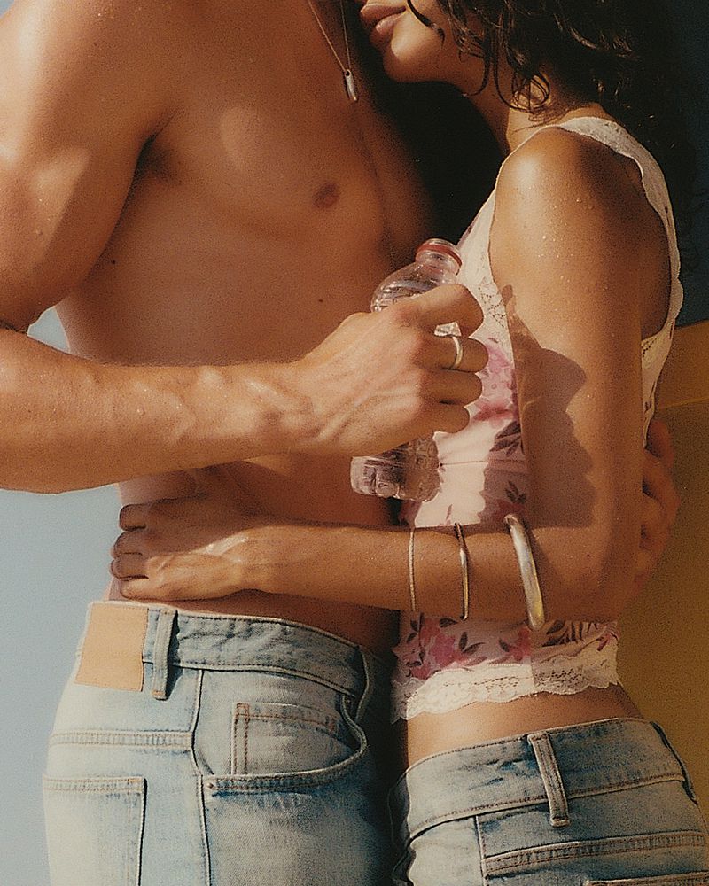 Close up shot of a couple embracing outdoors, with an adult male holding a water bottle and an adult female in a floral top and jeans.