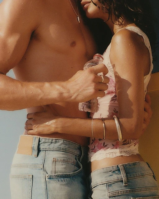Close up shot of a couple embracing outdoors, with an adult male holding a water bottle and an adult female in a floral top and jeans.