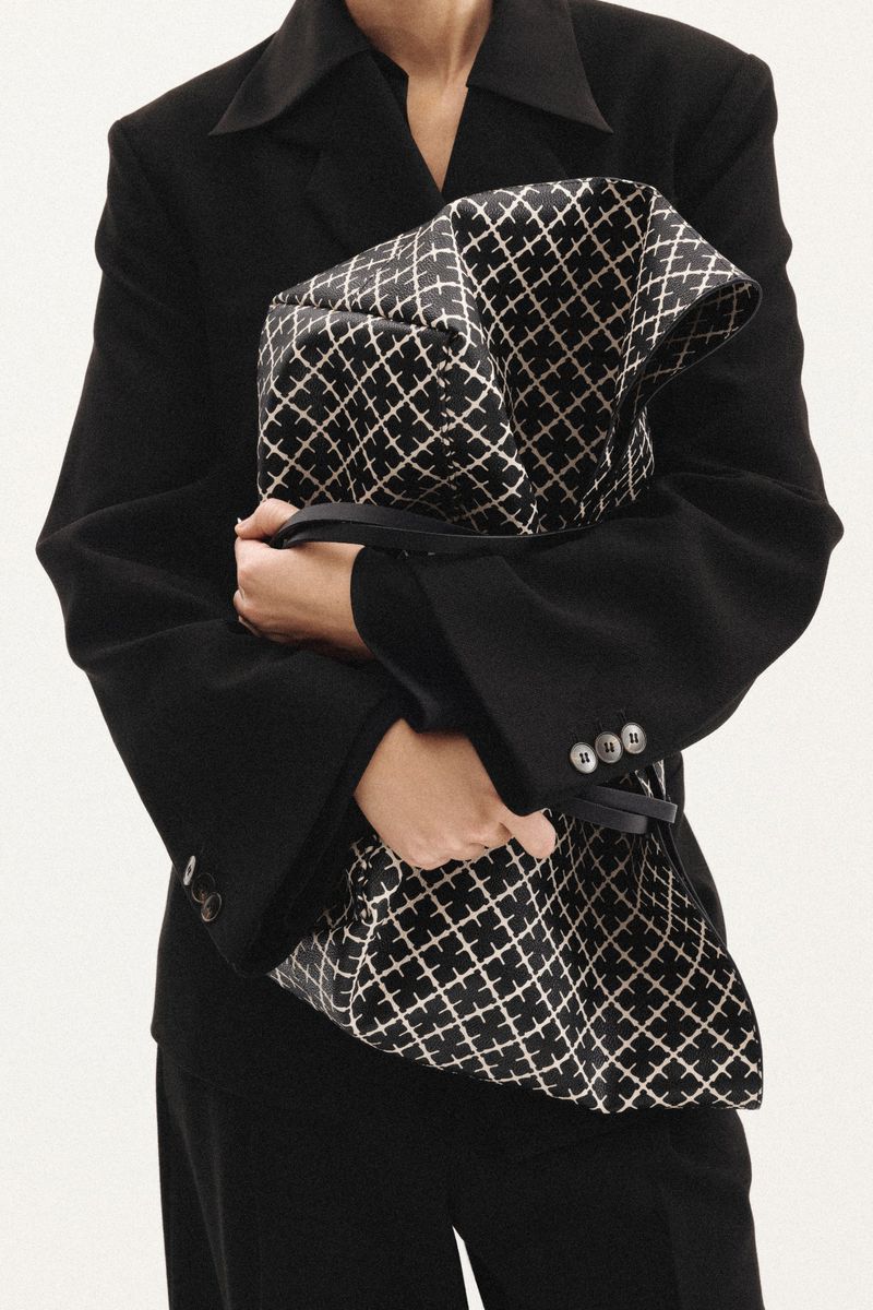 Close-up portrait of a person wearing a black blazer holding a large patterned bag for Malene Birger F/W 2025 Campaign