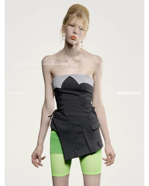 Fashionable woman in a gray corset and neon green shorts poses in front of a light backdrop.  Her makeup includes orange lipstick.